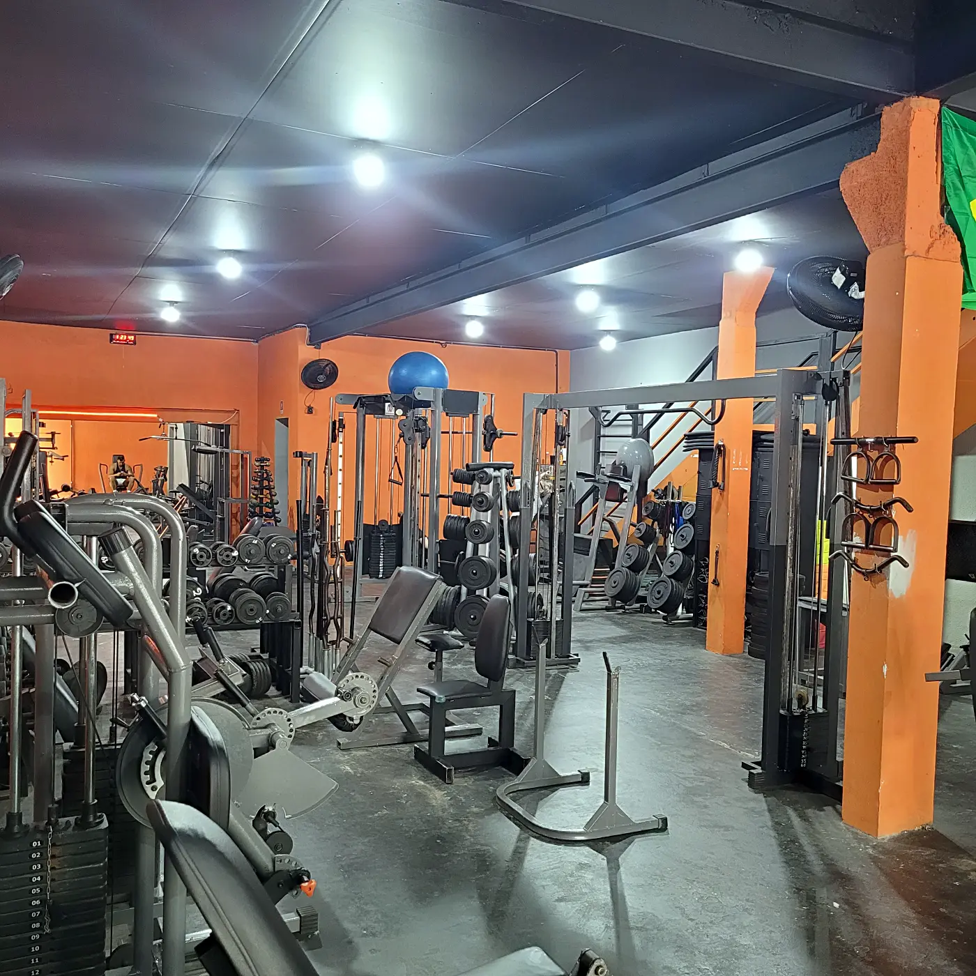 Salão de musculação da PowerLife 4D com estações de cabos, bola suíça e pilar laranja