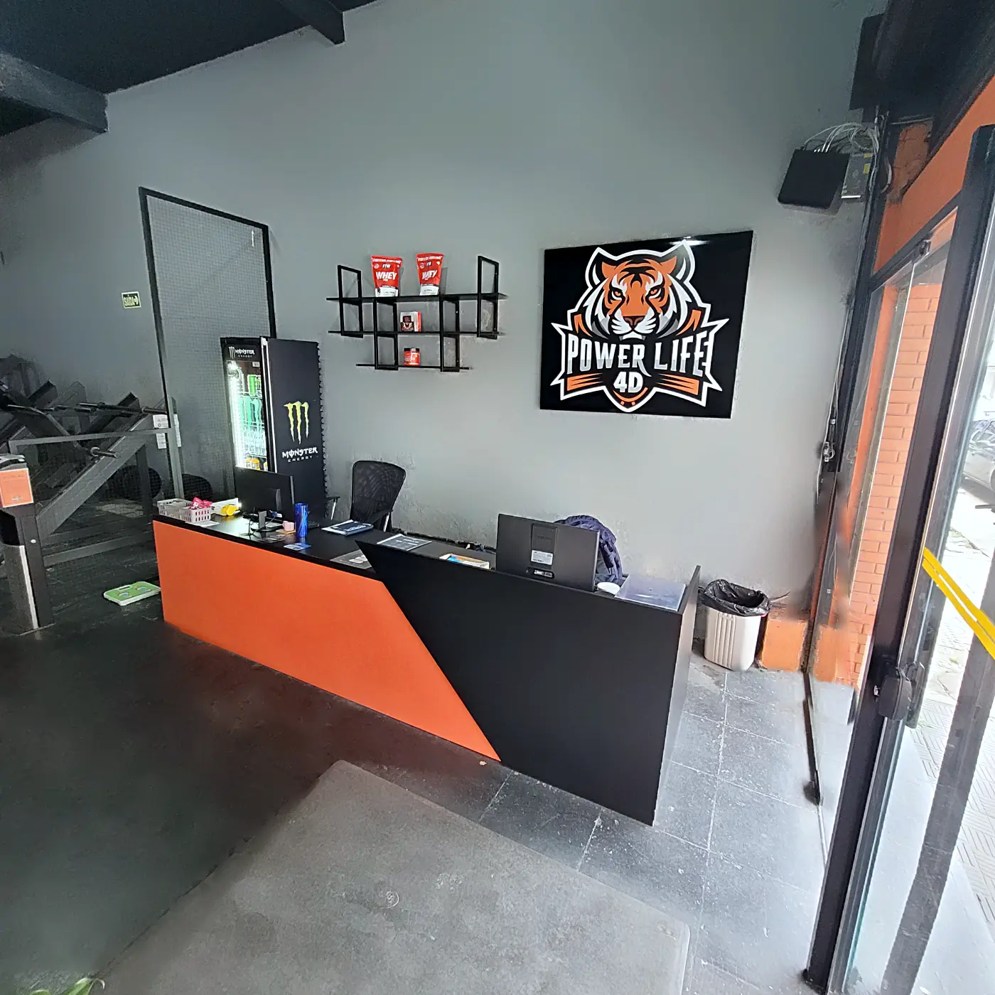 Recepção da PowerLife 4D com o logo do tigre na parede e balcão laranja e preto
