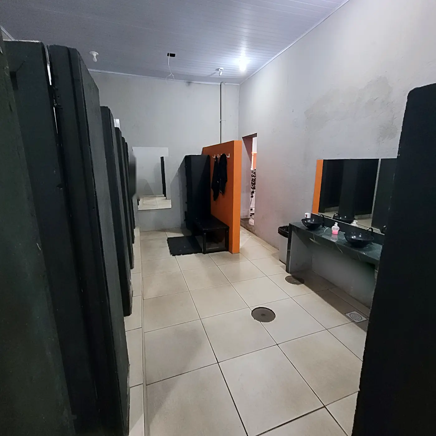 Vestiário visto de outro ângulo, com boxes de chuveiro quente e painel laranja de ganchos