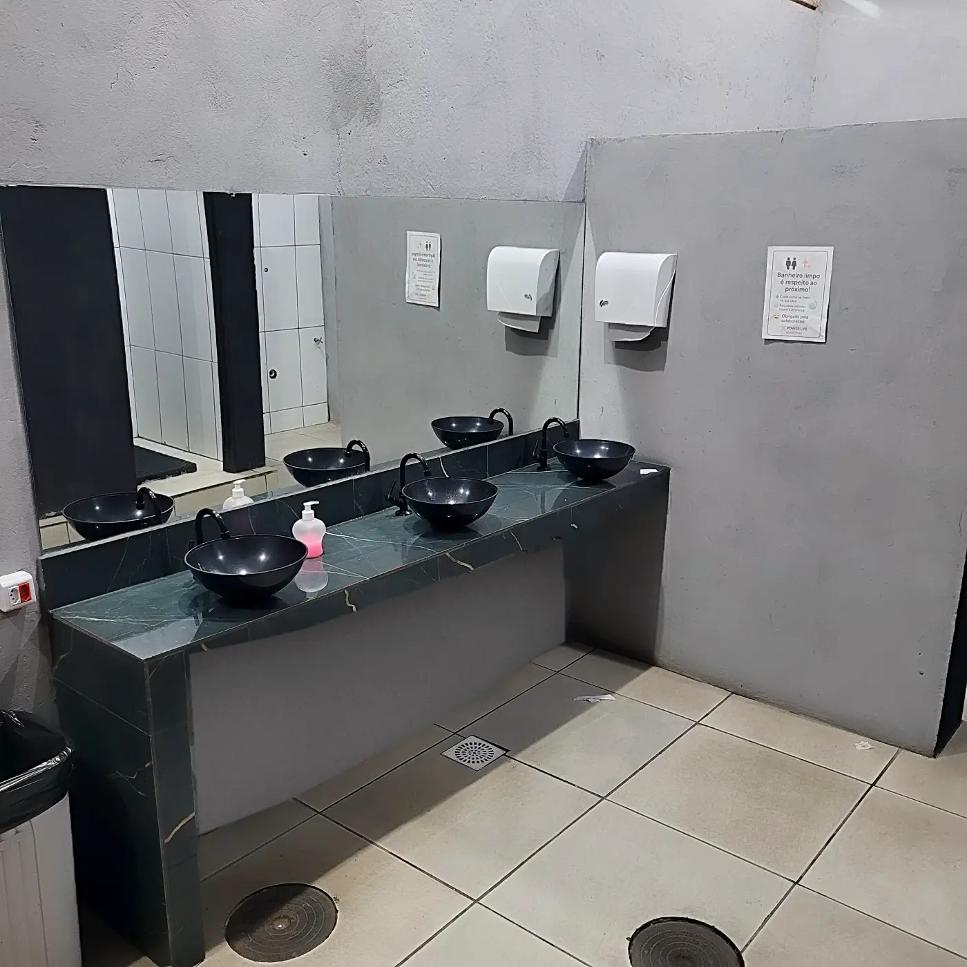 Bancada de pias com cubas pretas, espelho e porta-papel no vestiário